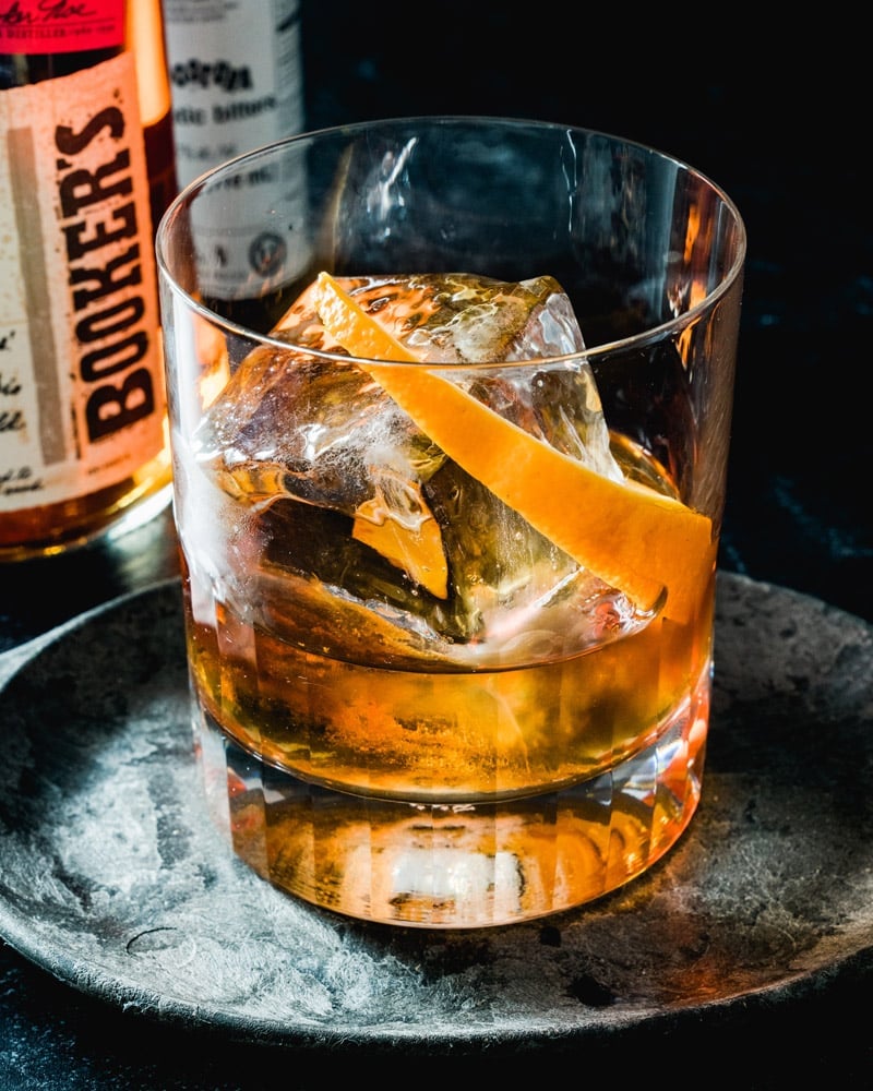 An old fashioned in a lowball glass with a large ice cube and an orange  peel