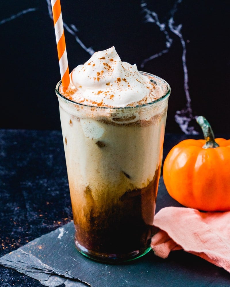 Iced Pumpkin Spice Latte in cup with straw and pumpkin in background