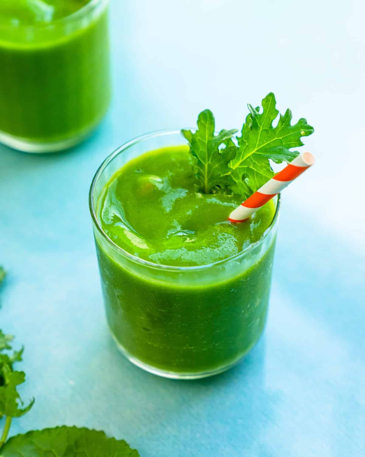 Kale Smoothie in a glass with straw and kale leaf garnish.