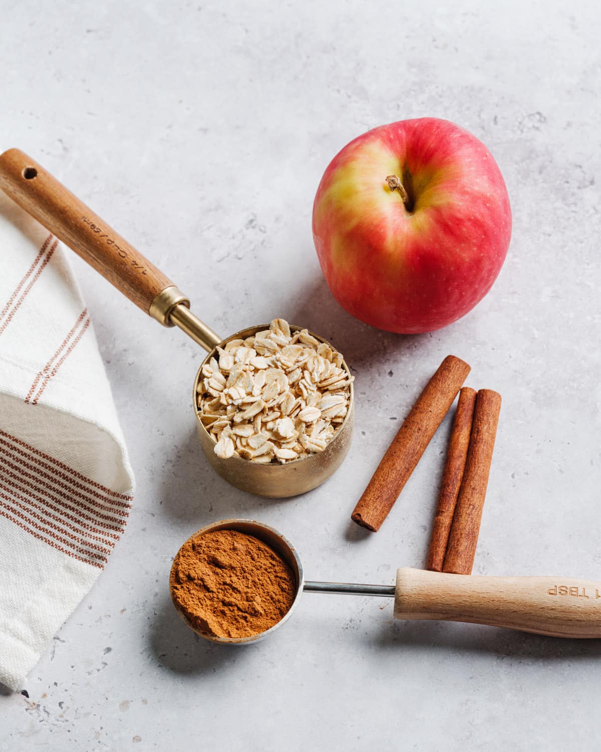 oats in a measuring cup, cinnamon in a spoon, apples